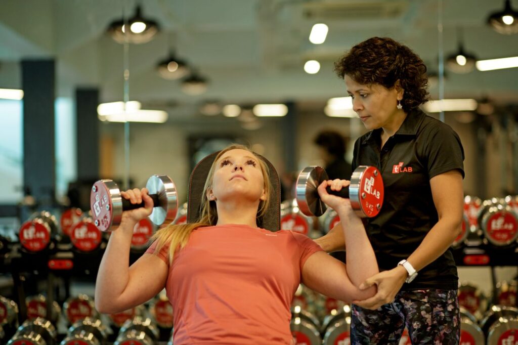 Two women engaged in weight training with dumbbells in a modern gym setting.